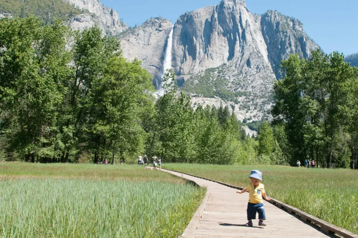 Mały chłopiec na ścieżce w Yosemite, w tle wodospad i trzy korony gór.
