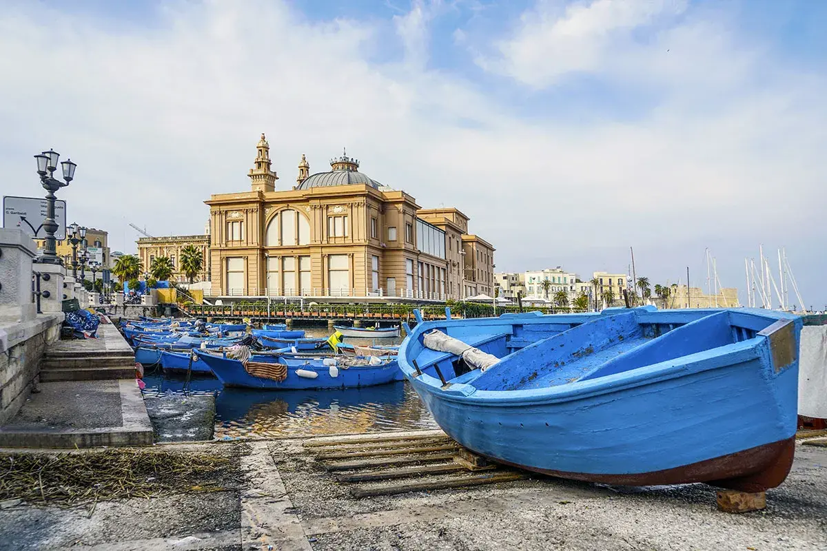 Barche blu nel porto del capoluogo della Puglia, con un edificio storico sullo sfondo.