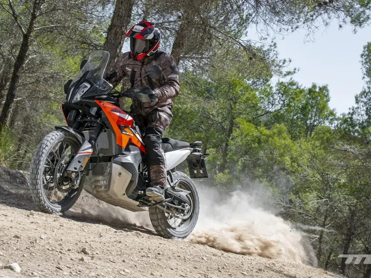 Motociclista con casco y equipo de aventura, derrapando una KTM 490 Adventure en un camino de tierra con polvo levantándose.