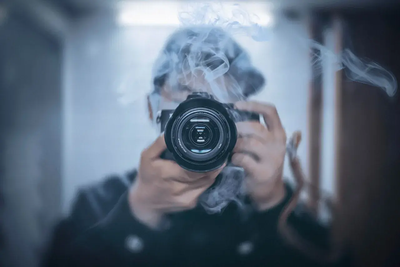 Osoba w kapturze śledzi i fotografuje gwiazdy przez obiektyw aparatu, otoczona mgiełką dymu.