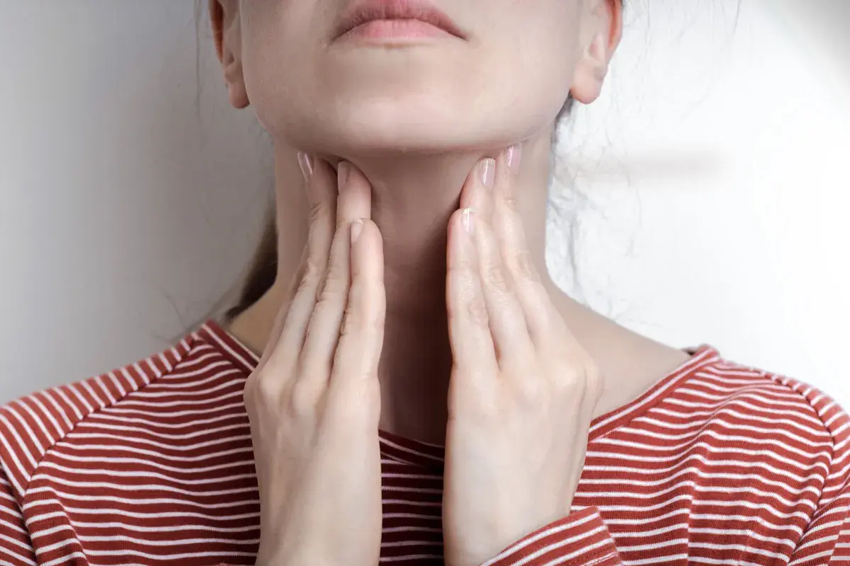 Femme touchant sa gorge, possible symptôme mononucléose. Douleur ou gonflement au cou.