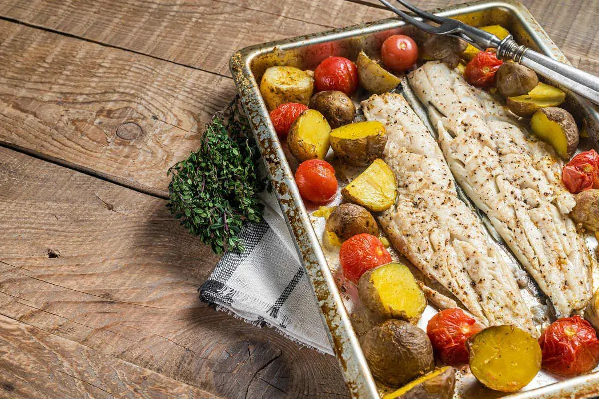 Coda di rospo al forno con patate e pomodorini su un tagliere di legno rustico, guarnita con timo fresco.