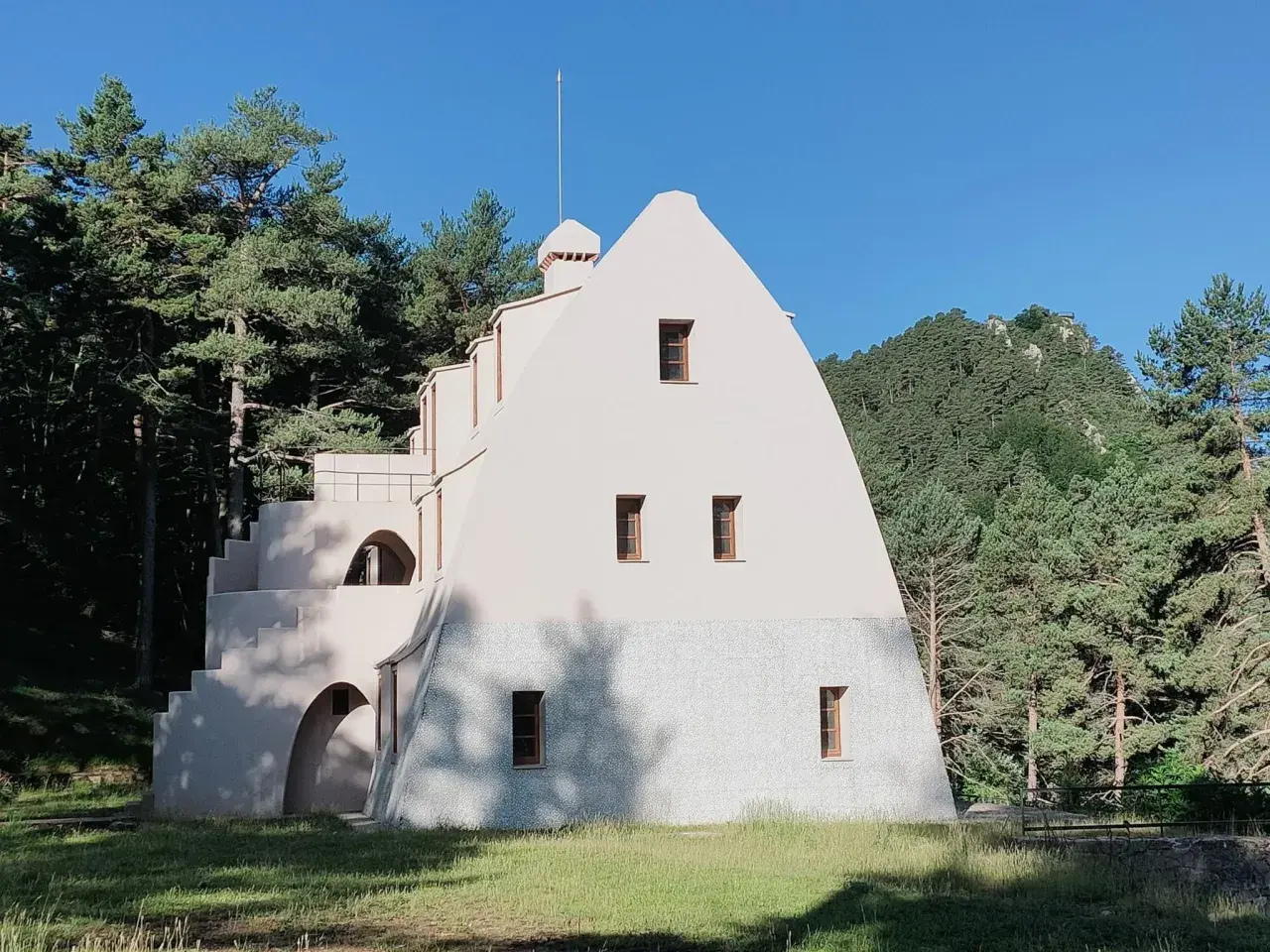 Edificio singular en la Serra de Catllaras, rodeado de pinos y con un cielo azul intenso.