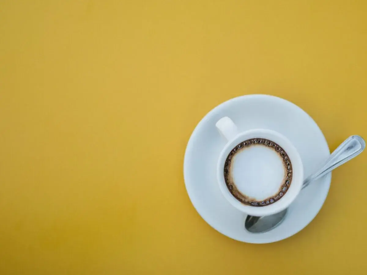 En vit kopp med kaffe macchiato står på en tefat med en sked. En perfekt start på dagen, det är vad macchiato betyder.
