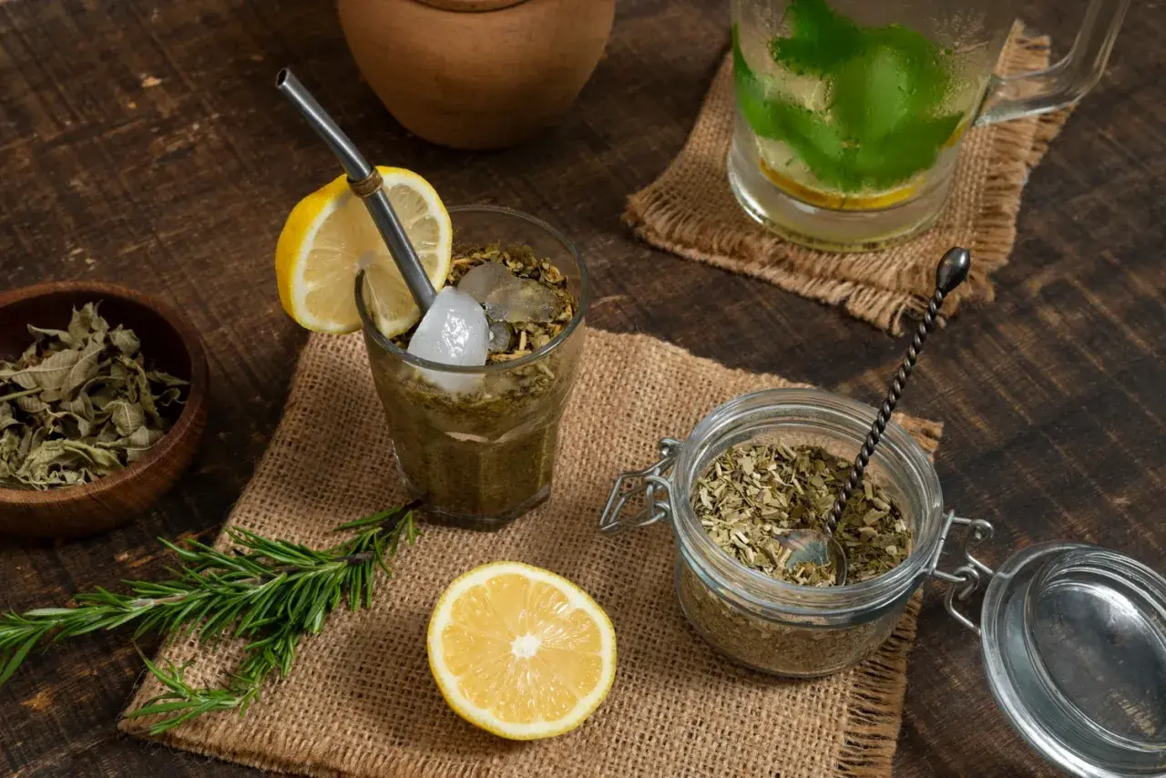 Orzeźwiająca yerba mate cytrynowa z lodem i rozmarynem, obok słoik z suszem i cytryna.