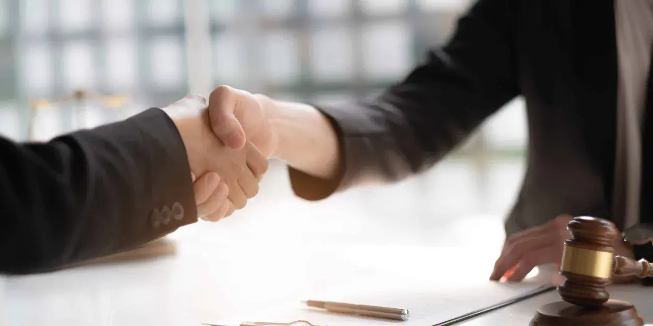 Poignée de main entre deux avocats, symbolisant un accord ou un **départage prudhomme**. Un maillet de juge est visible sur la table.