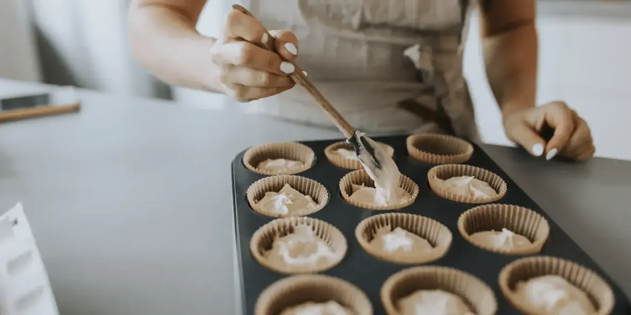 En person fyller muffinsformar med smet. Bra baka tips för perfekta muffins.