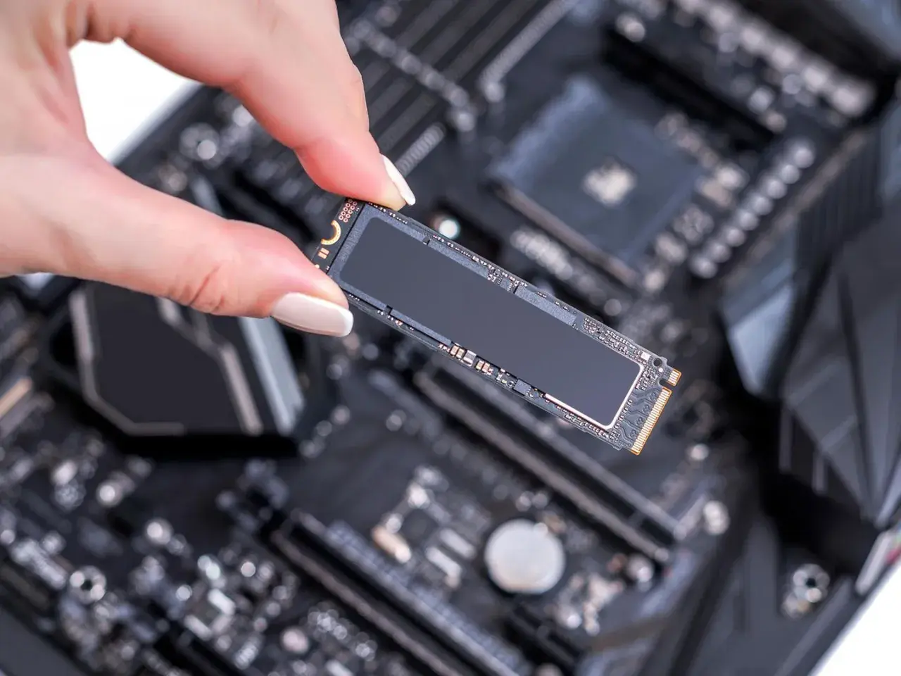 Eine Hand hält eine M.2 SSD, bereit für den Einbau in einen SSD-Steckplatz auf einem Computer-Motherboard.