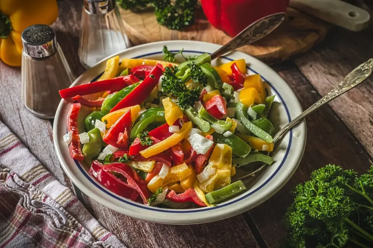 Bunter Paprika Salat mit Zwiebeln und Petersilie, serviert in einer Schüssel mit zwei Löffeln.