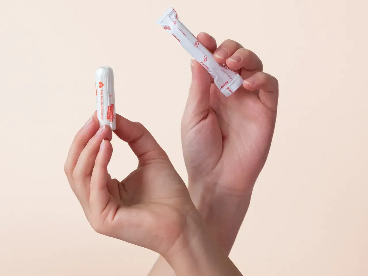 Zwei Hände halten Tampons. Einer ist ausgepackt, der andere noch in seiner Hülle. So sieht ein Tampon aus.