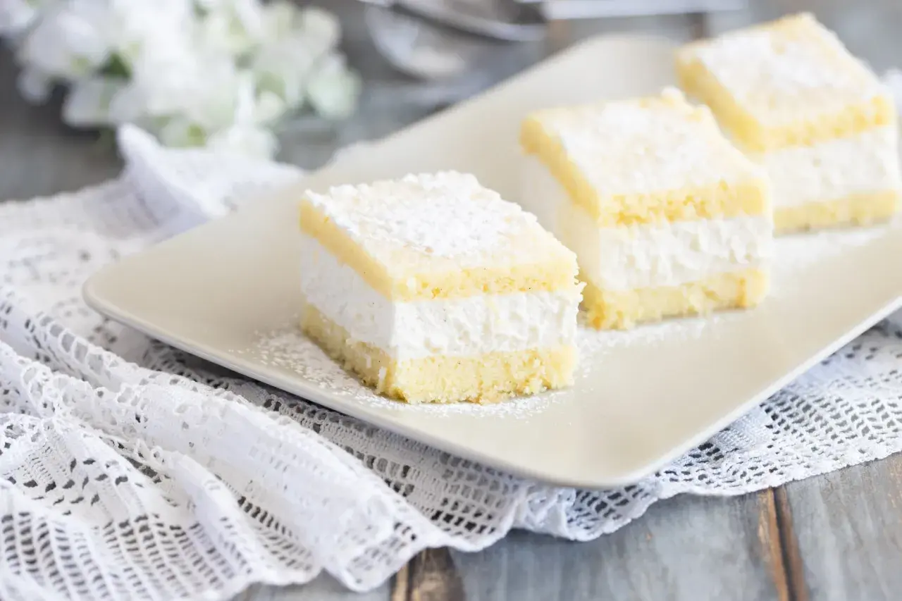 Tre soffici fette di torta Kinder Paradiso, cosparse di zucchero a velo, su un piatto bianco.