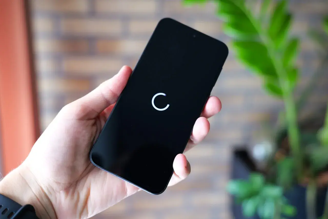 Dłoń trzyma czarny smartfon z białym kółkiem ładowania na ekranie.