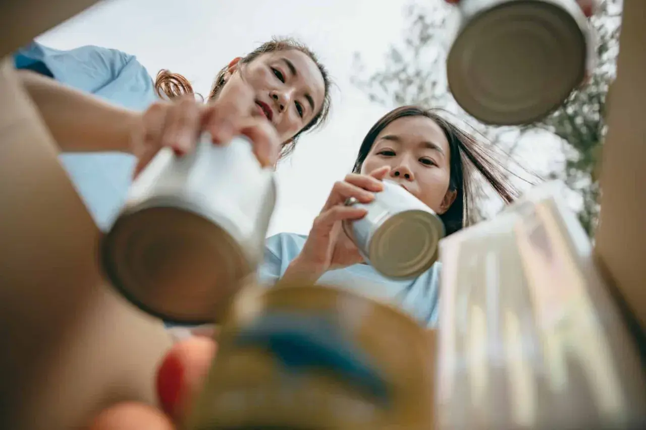 Two young women participate in voluntary community service, sorting cans for recycling.