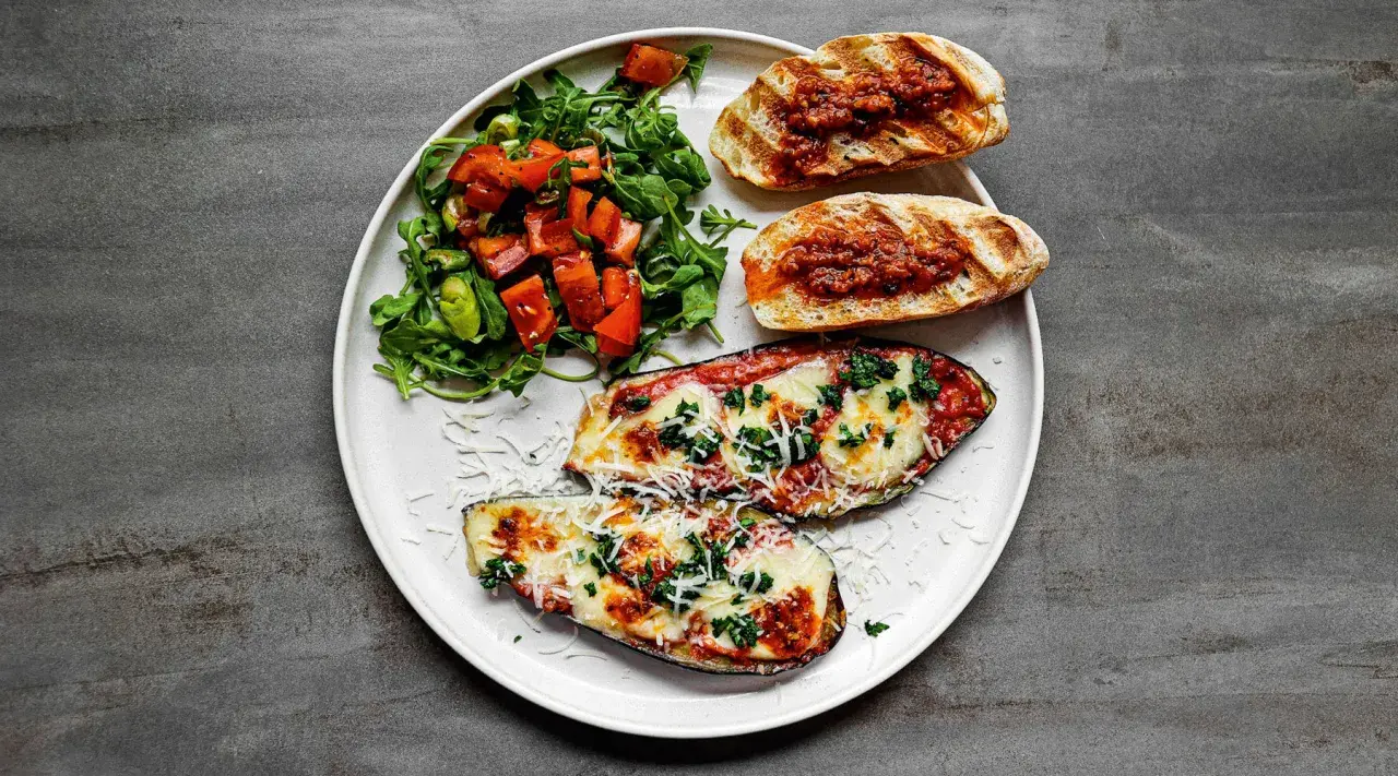 Gegrillte Auberginenhälften mit geschmolzenem Käse, Bruschetta und einem frischen Salat – perfekt für einen italienischen Abend.