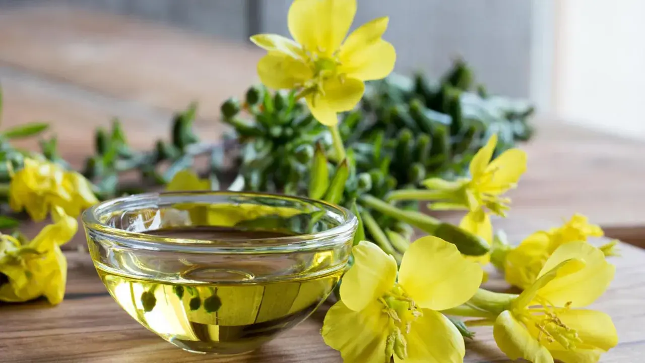 Aceite de onagra en un cuenco de cristal rodeado de flores amarillas, destacando sus beneficios naturales.