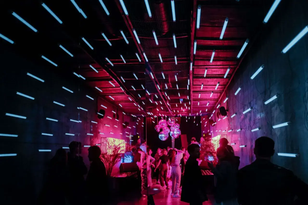 Ein **Partyraum gestalten** mit Neonröhren und Discokugeln. Menschen tanzen im pulsierenden Licht.