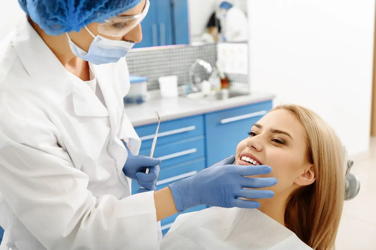 Dentystka bada uśmiechniętą pacjentkę, by wykluczyć zapalenie okostnej i ropień zęba.