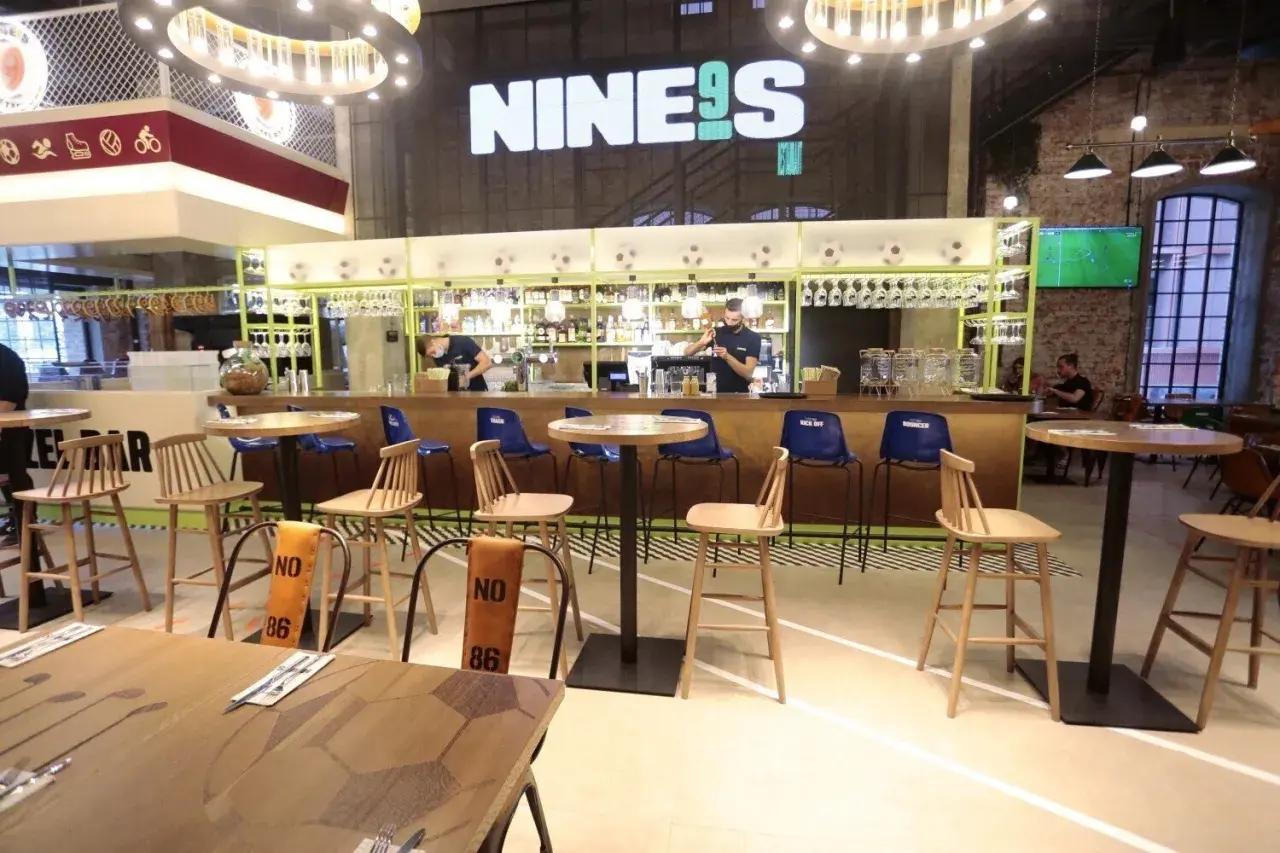 Wnętrze restauracji Lewandowskiego "NINE9S" z barem, stołkami i stołami.