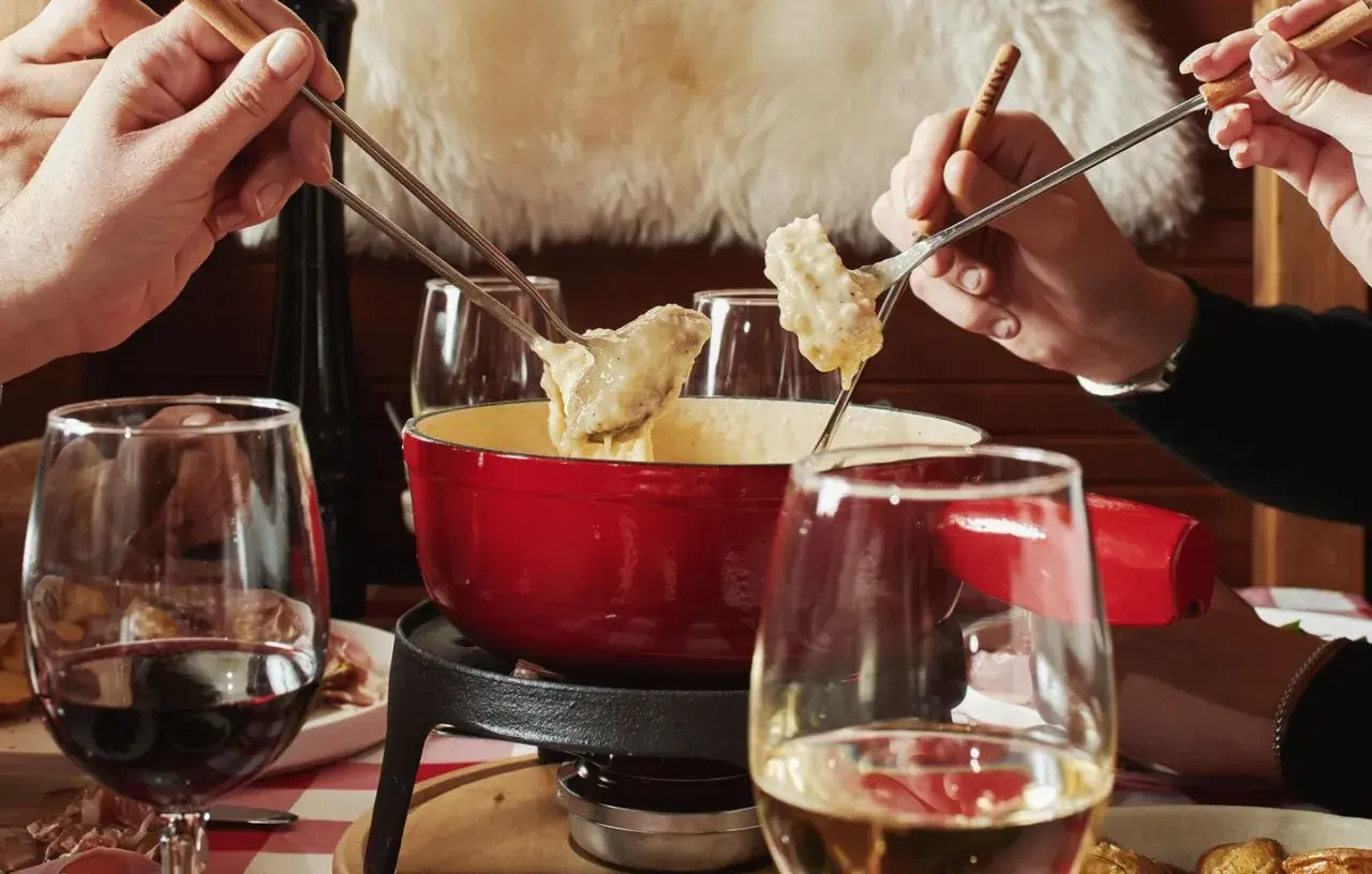 Des mains plongent des morceaux de pain dans une fondue pyrénéenne crémeuse, un moment convivial autour d'un plat réconfortant.