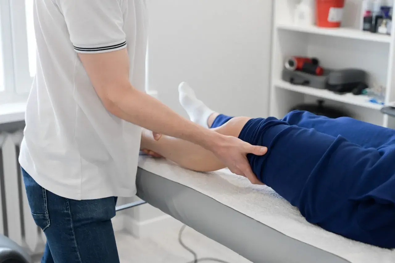 Fizjoterapeuta wykonuje masaż nogi pacjenta leżącego na kozetce.