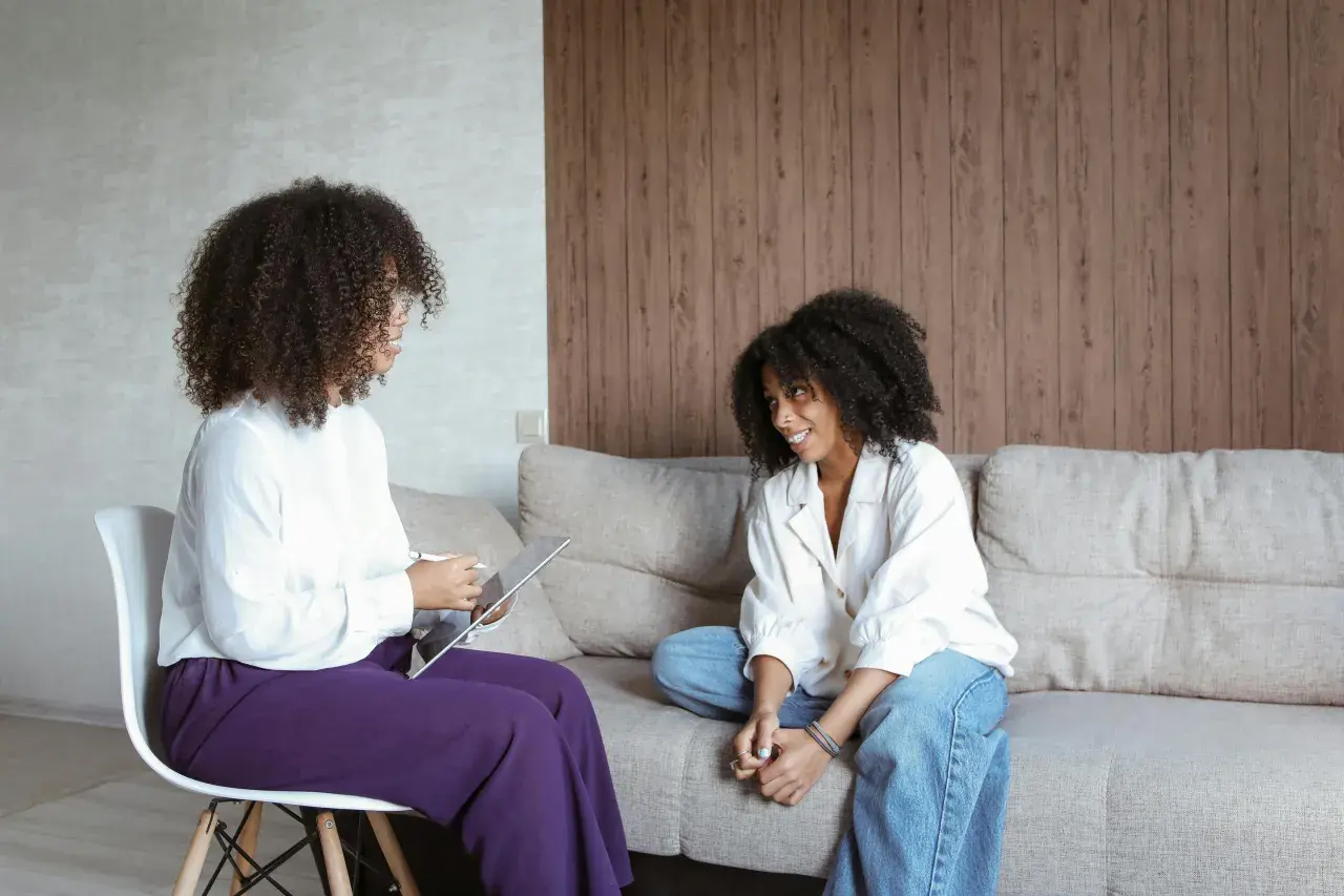 Due donne parlano in un ambiente accogliente. Una, seduta su una sedia, usa un tablet, mentre l'altra è rilassata sul divano. Potrebbe essere una sessione di psicoterapia breve strategica cos'è.