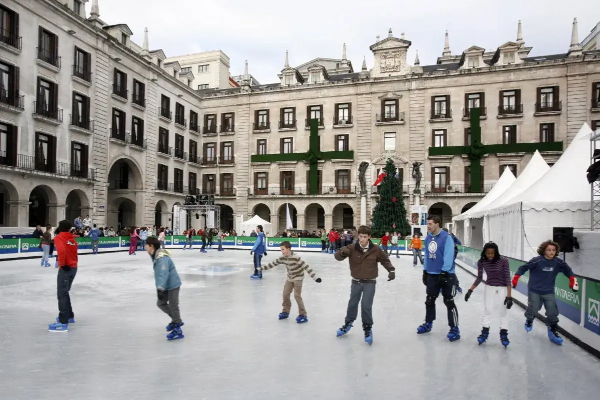 Gente patinando en la pista de hielo de Santander, con un árbol de Navidad y edificios históricos de fondo.