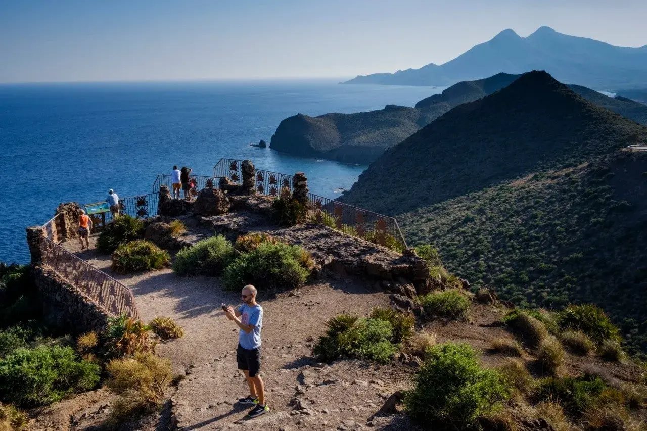 Un hombre toma una foto en un mirador con vistas a la cala de enmedio y montañas.