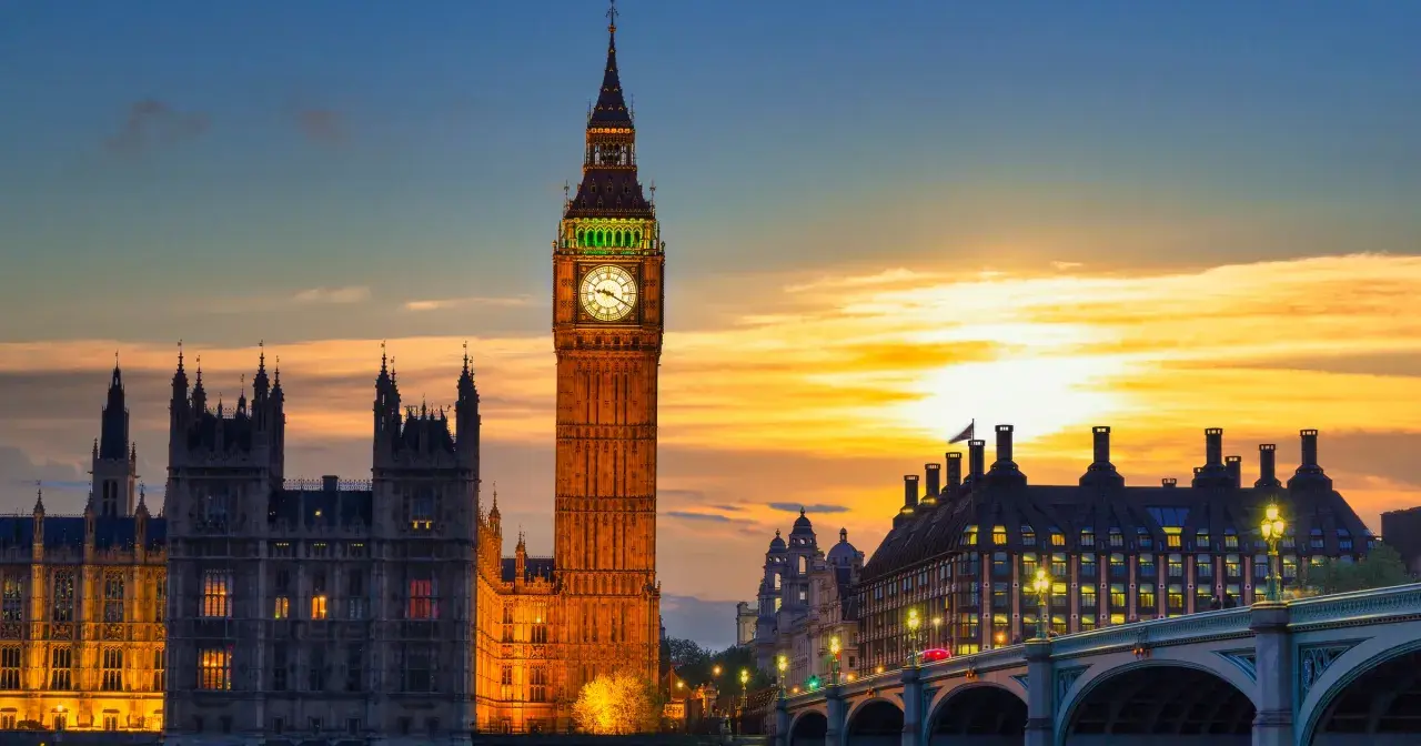 Wieża zegarowa Big Ben w Londynie o zachodzie słońca, z Parlamentem i mostem w tle.