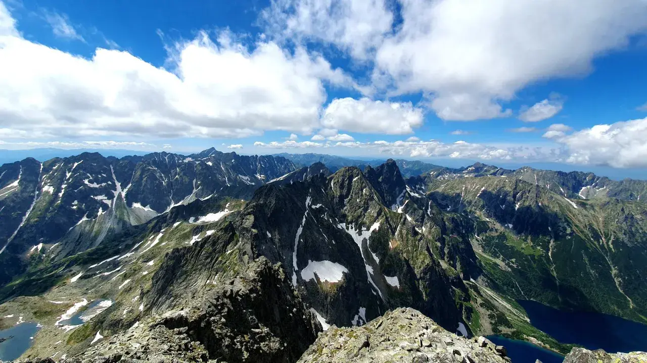 Widok na pasmo górskie Rysy, gdzie szlak wije się wśród skalistych zboczy i resztek śniegu.