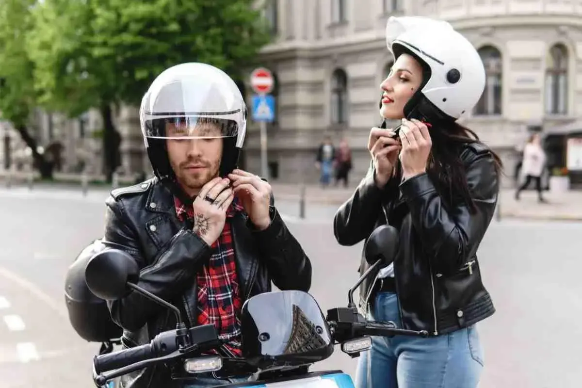 Coppia in moto, lui sistema il suo casco nuovo che fa male, lei il suo.