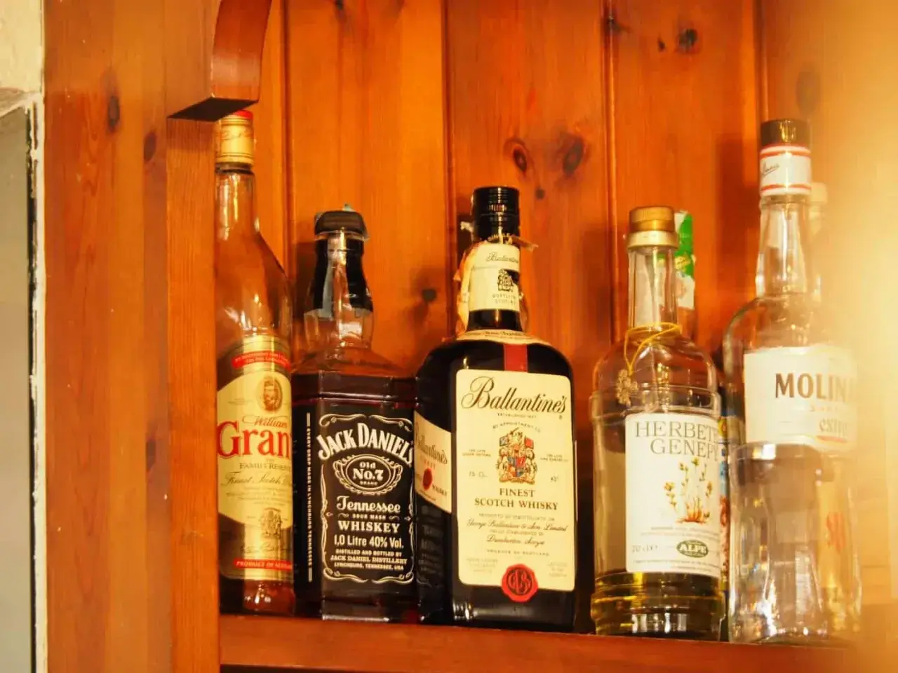 Butelki whisky na drewnianej półce. Zwróć uwagę na zmętnienie i osad w starych butelkach, by rozpoznać objawy zepsutej whisky.