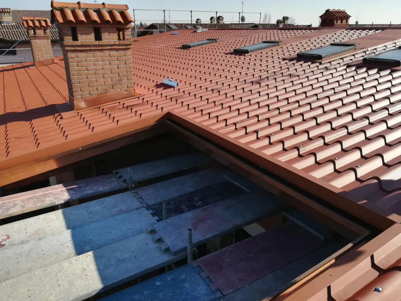 Tetto alla piemontese con tegole rosse, comignoli in mattoni e lucernari. In primo piano, impalcature per lavori di ristrutturazione.
