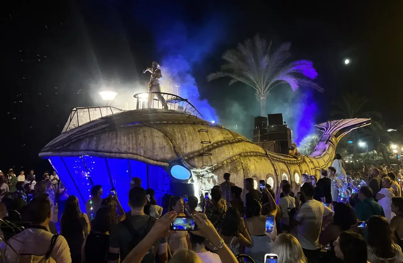 Una gran ballena mecánica ilumina la noche en una fiesta de los 90 en Zaragoza. El público, con móviles en mano, celebra el espectáculo.
