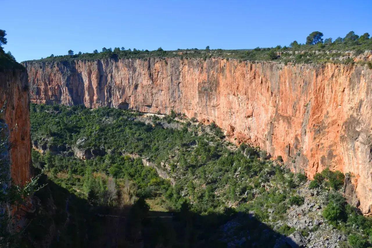 Impresionante cañón con paredes rojizas y vegetación verde. Los puentes colgantes de Chulilla se asoman entre la naturaleza.