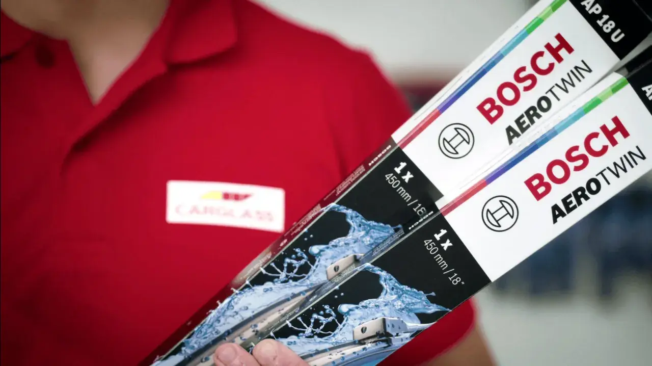 Person i röd pikétröja med Carglass-logga håller upp två paket med Bosch Aerotwin torkarblad.