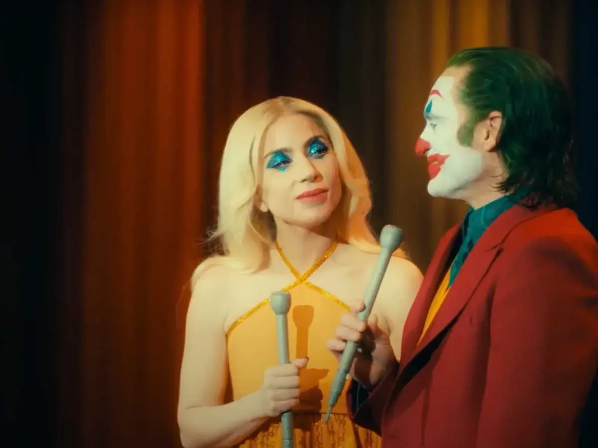 La femme du Joker, avec son maquillage bleu scintillant, semble chanter face à lui, le clown au visage blanc et rouge.