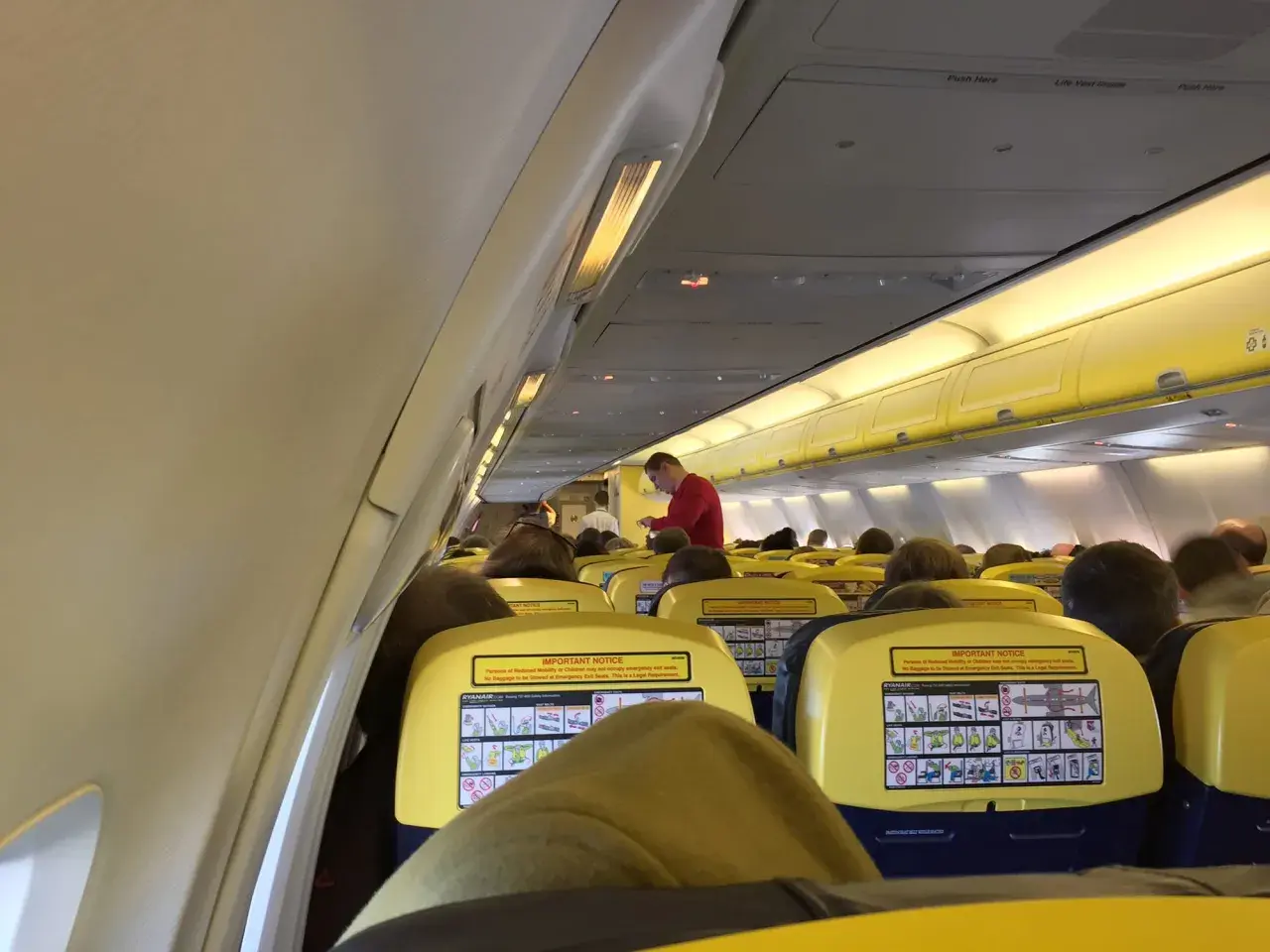 Wnętrze samolotu Ryanair, pasażerowie siedzą w rzędach. Na oparciach siedzeń widoczne są żółte tabliczki z instrukcjami bezpieczeństwa, co może uspokoić osoby zastanawiające się, czy Ryanair jest bezpieczny.