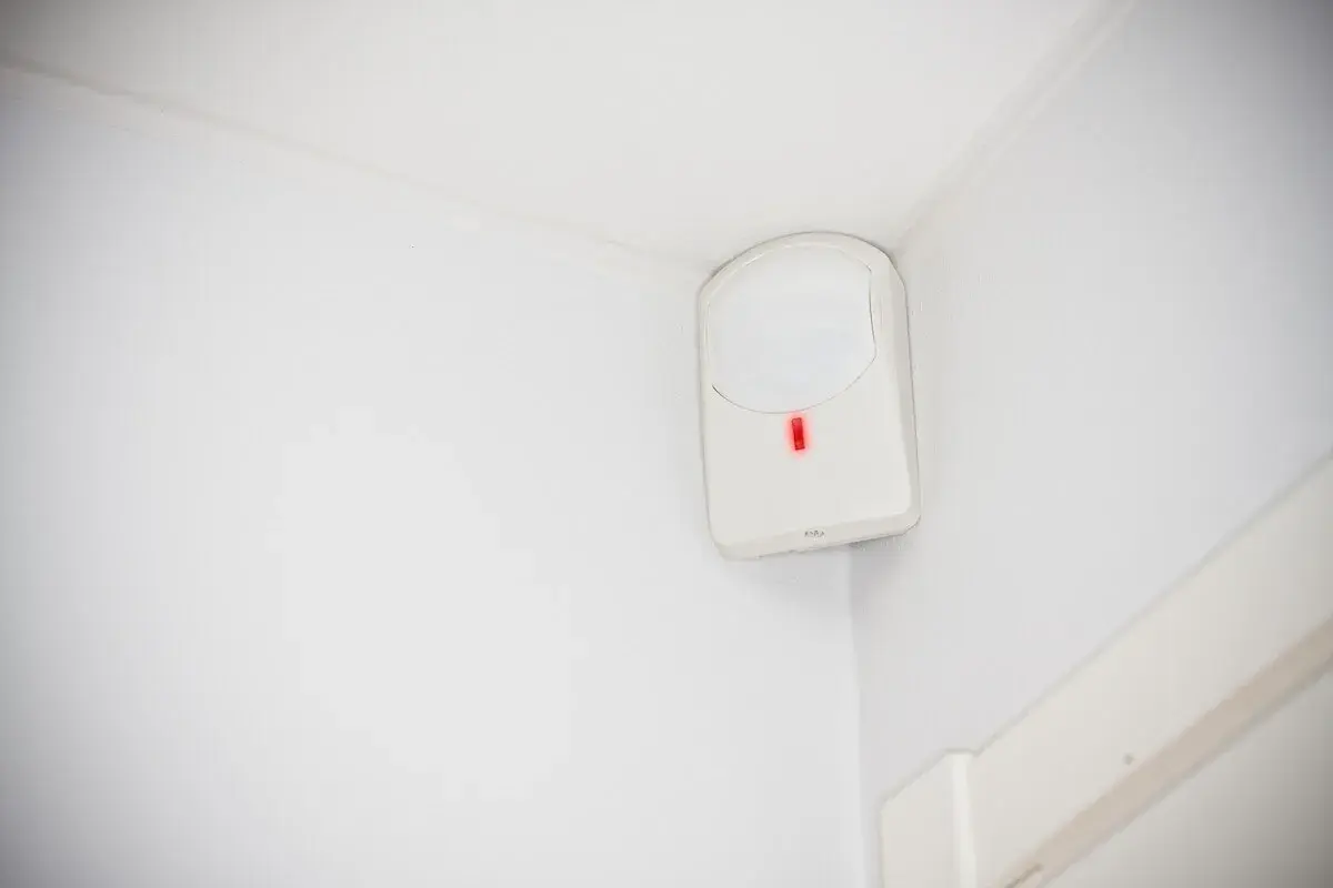 Detector de presencia blanco en esquina de pared, con luz roja encendida. Así es como funciona un detector de presencia.