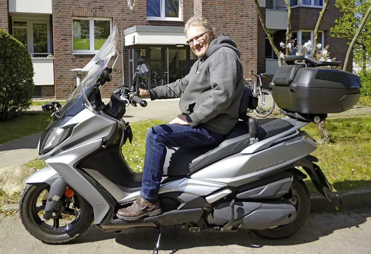 Mann auf silbernem Kymco New Downtown 350i, der über Probleme nachdenkt.