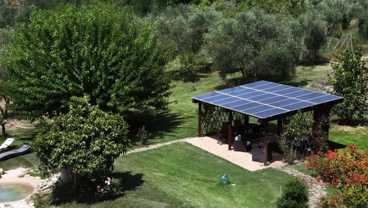 Un pergolato con pannelli fotovoltaici a terra in giardino, in linea con la normativa, offre ombra e energia pulita.