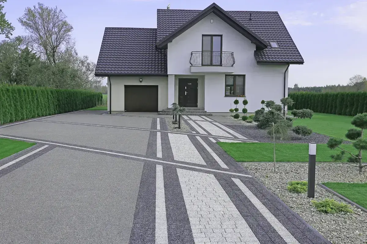 Nowoczesny podjazd z kamienia prowadzi do białego domu z garażem.