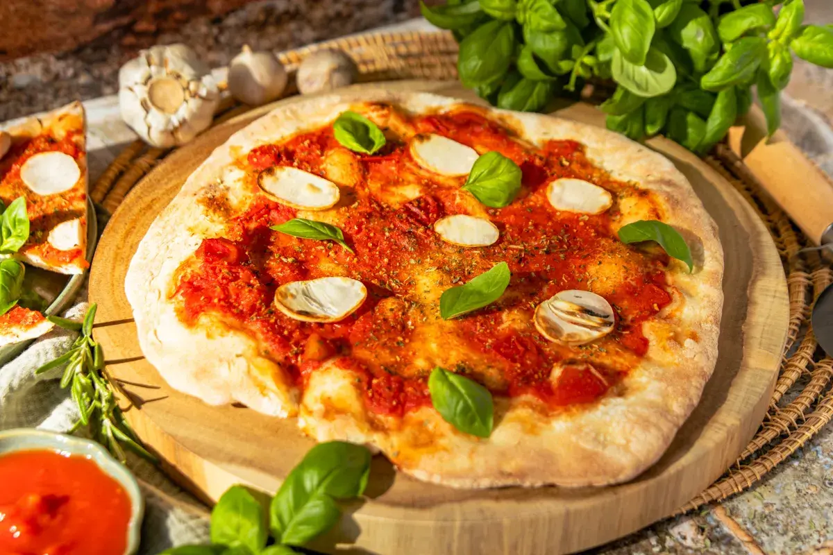 Eine köstliche Pizza Marinara mit Tomatensauce, Knoblauchscheiben und frischem Basilikum auf einem Holzbrett.