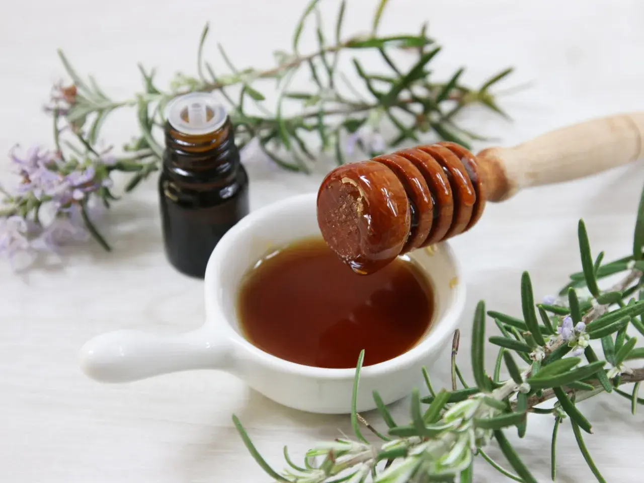 Un vasetto di vetro scuro, un cucchiaio di miele che cola e rametti di rosmarino fresco: ingredienti per un estratto di rosmarino fai da te.