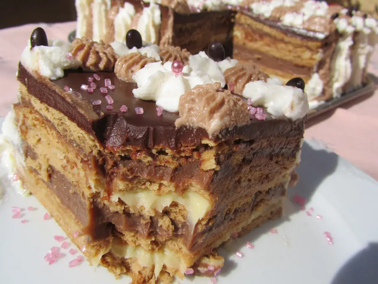 Tarta de galletas de la abuela de toda la vida, con capas de crema y chocolate, decorada con nata y granillo rosa.