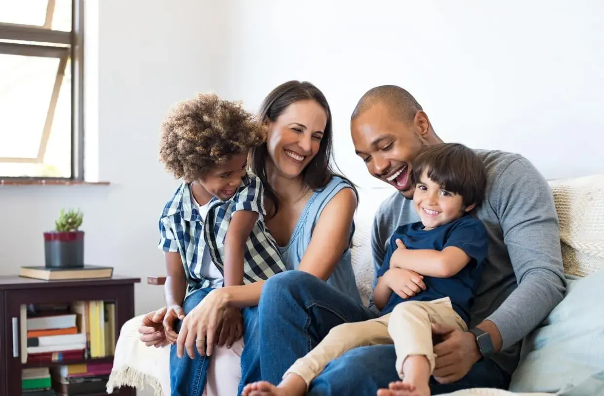 Famille souriante sur un canapé, profitant d'un moment de joie. Ce bonheur est rendu possible grâce à un **prêt conventionné** qui leur a permis d'acquérir leur foyer.