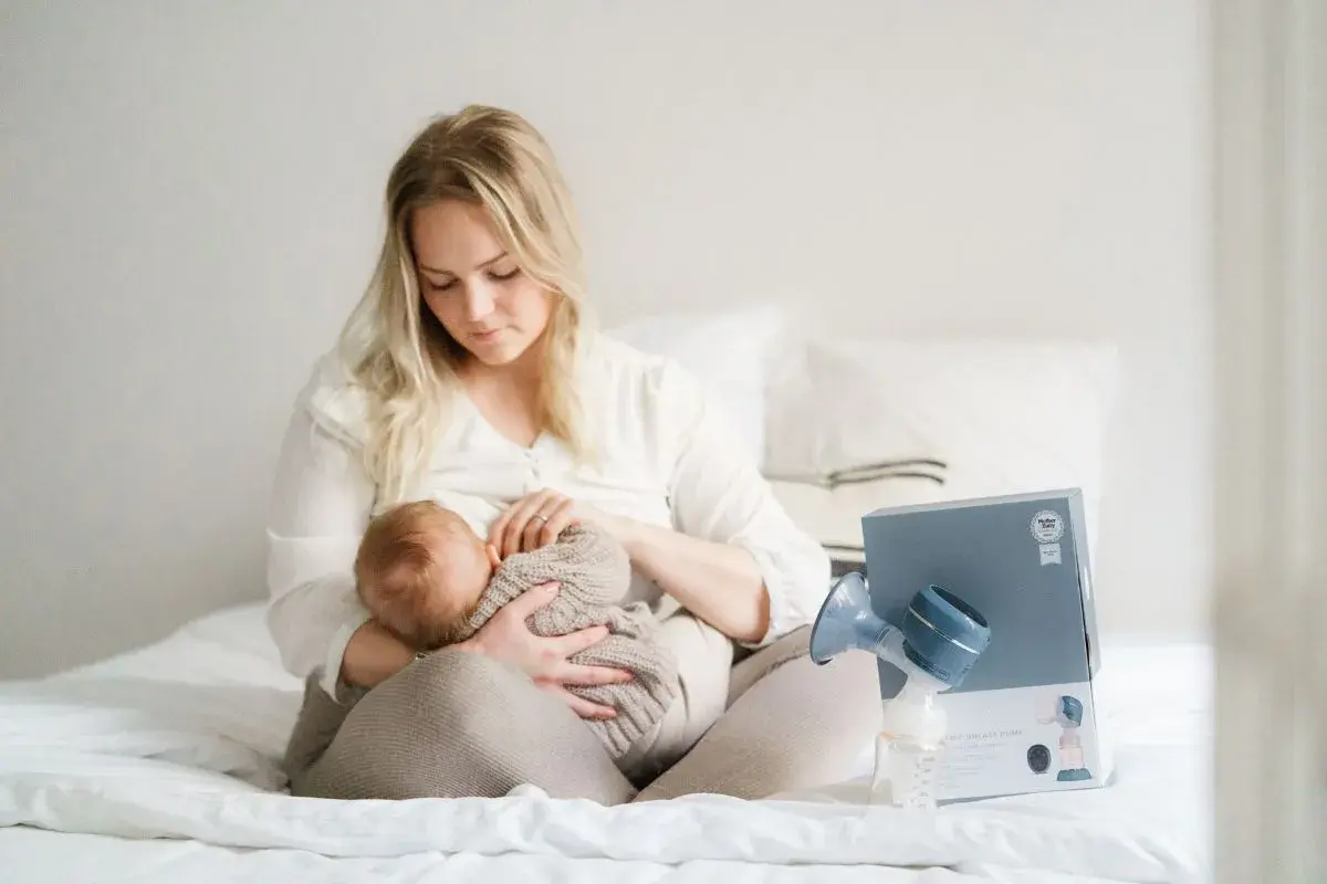 En mamma ammar sitt lilla barn. Bredvid dem står en bröstpump och dess förpackning.