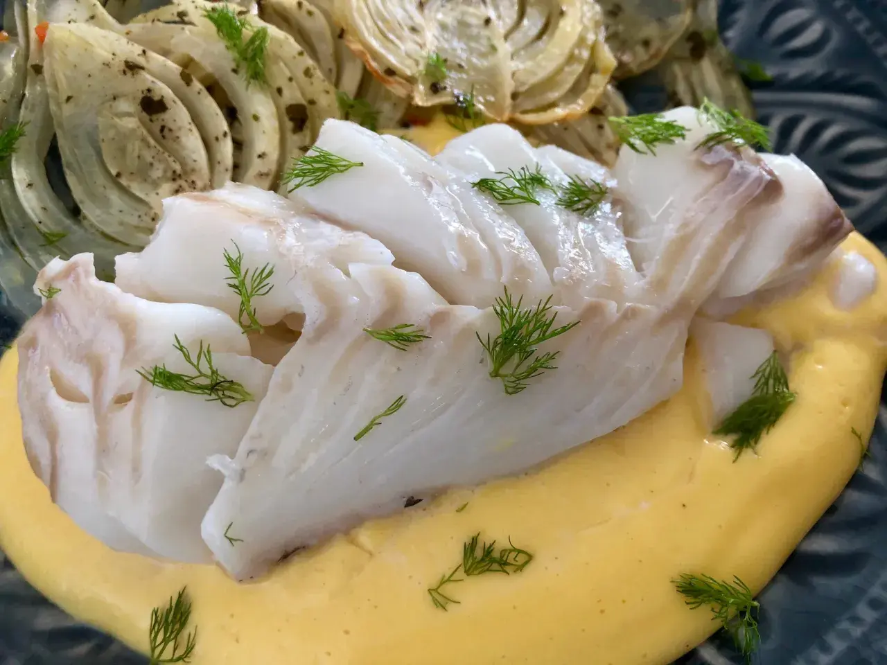 Saftigt vit fisk serveras med krämig sås och ugnsbakad fänkål, garnerad med dill.
