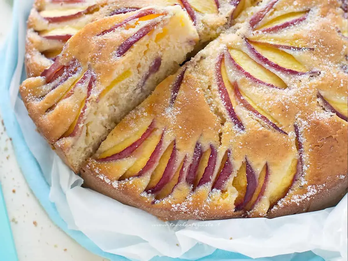 Una fetta di torta di pesche morbidissima, con pesche affettate disposte a raggiera sulla superficie dorata e cosparsa di zucchero a velo.