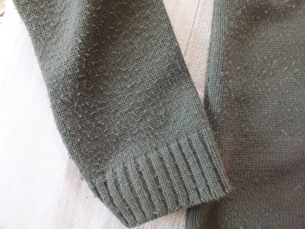 Zielony sweter z dzianiny, na którym widać, czy bawełna się kulkuje. Włókna tworzą drobne kuleczki na powierzchni materiału.
