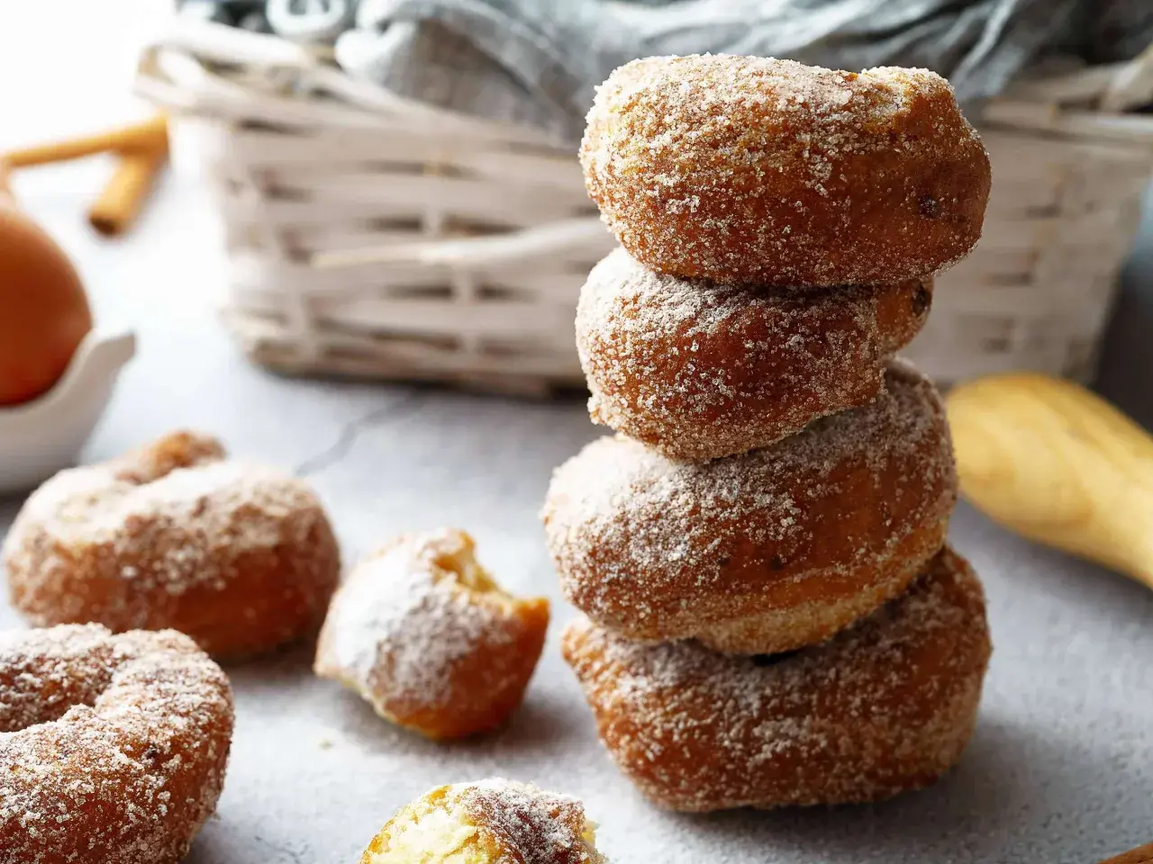 Gestapelte, zuckerglasierte Apfelkrapfen aus dem Airfryer, daneben weitere Krapfen und ein Ei.
